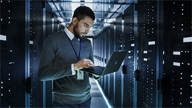 a man standing in a datacenter using a laptop